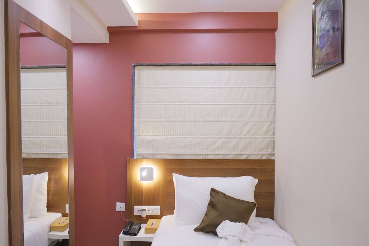 Ett hotellrum med en säng, sängbord, en spegel och ett fönster med persienner.
