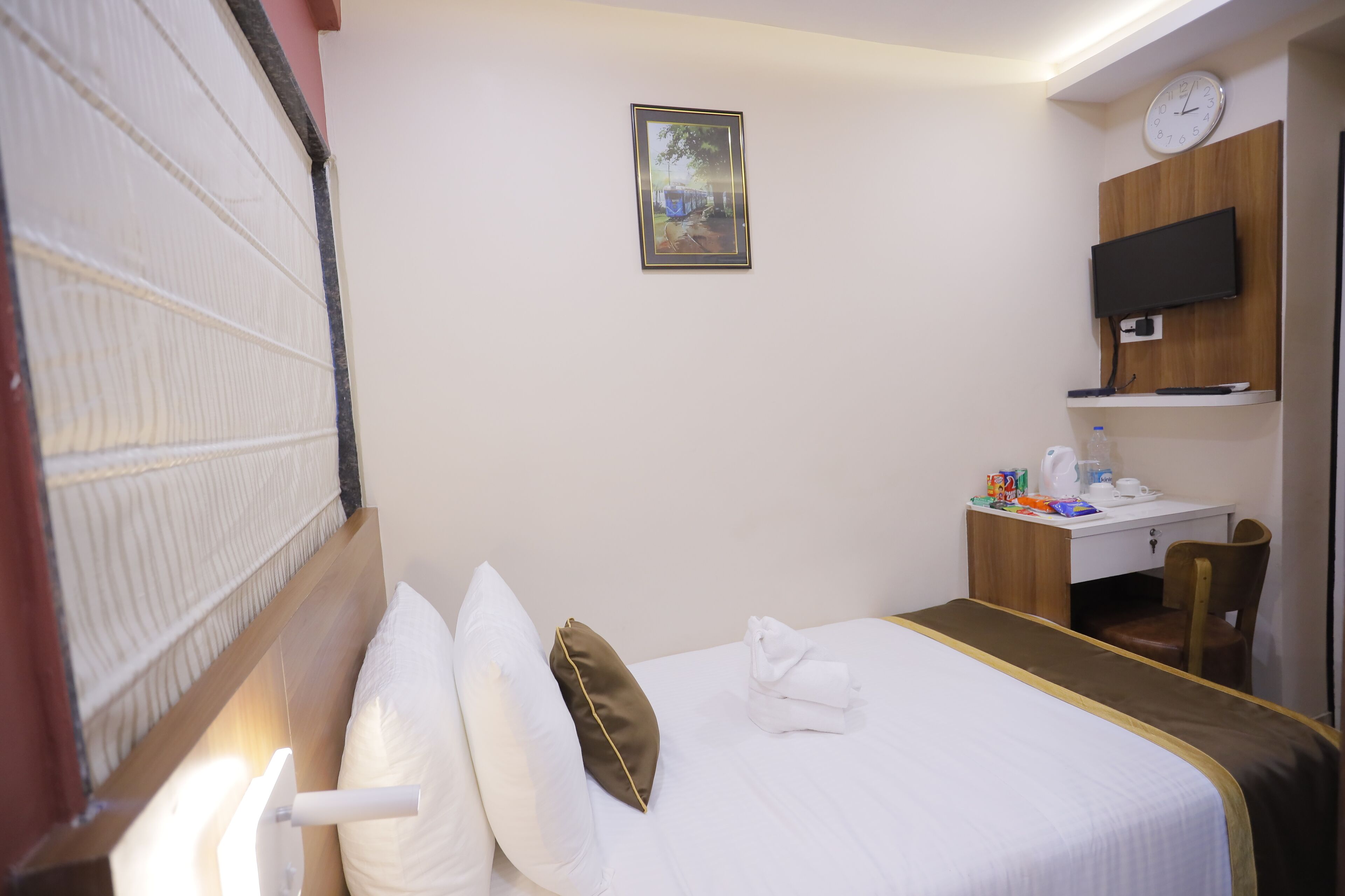 Una habitación de hotel con cama, escritorio, silla, televisor y un reloj en la pared.
