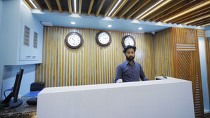 A reception area with a wooden slatted wall, three clocks, and a desk with a computer and phone.
