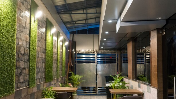 A modern indoor space with wooden tables and chairs, green wall accents, and a staircase leading to an upper level.