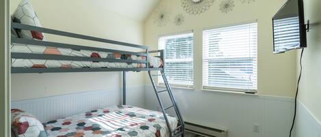A bunk bed room with a TV mounted on the wall, a window with blinds, and decorative wall art.