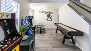 Um quarto com mesa de bilhar, máquina de pinball e um mural com um urso.