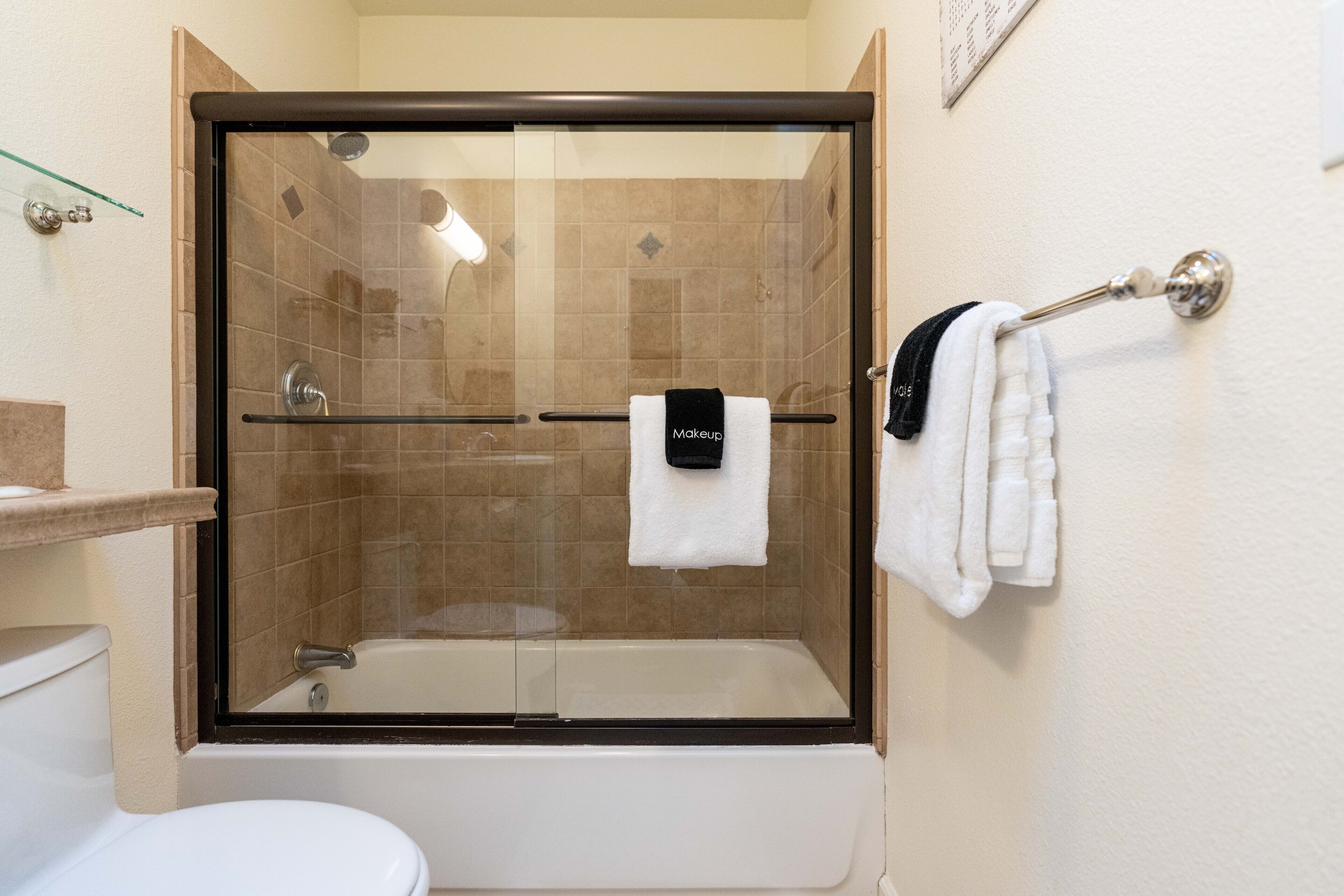 A bathroom with a glass-enclosed shower, a white bathtub, and a toilet.