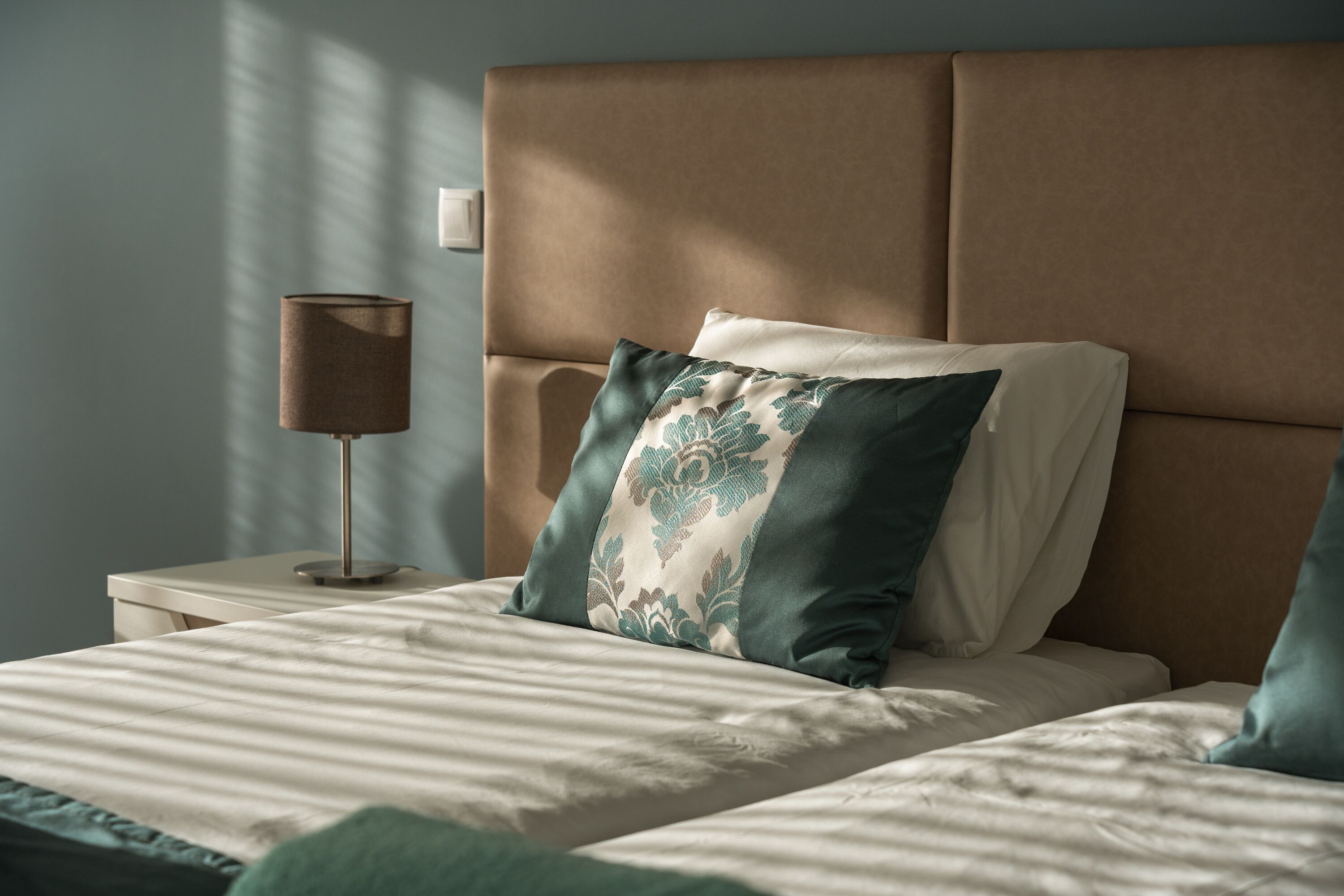 Un lit bien fait, avec une tête de lit, une lampe de chevet et un oreiller orné d’un motif floral.