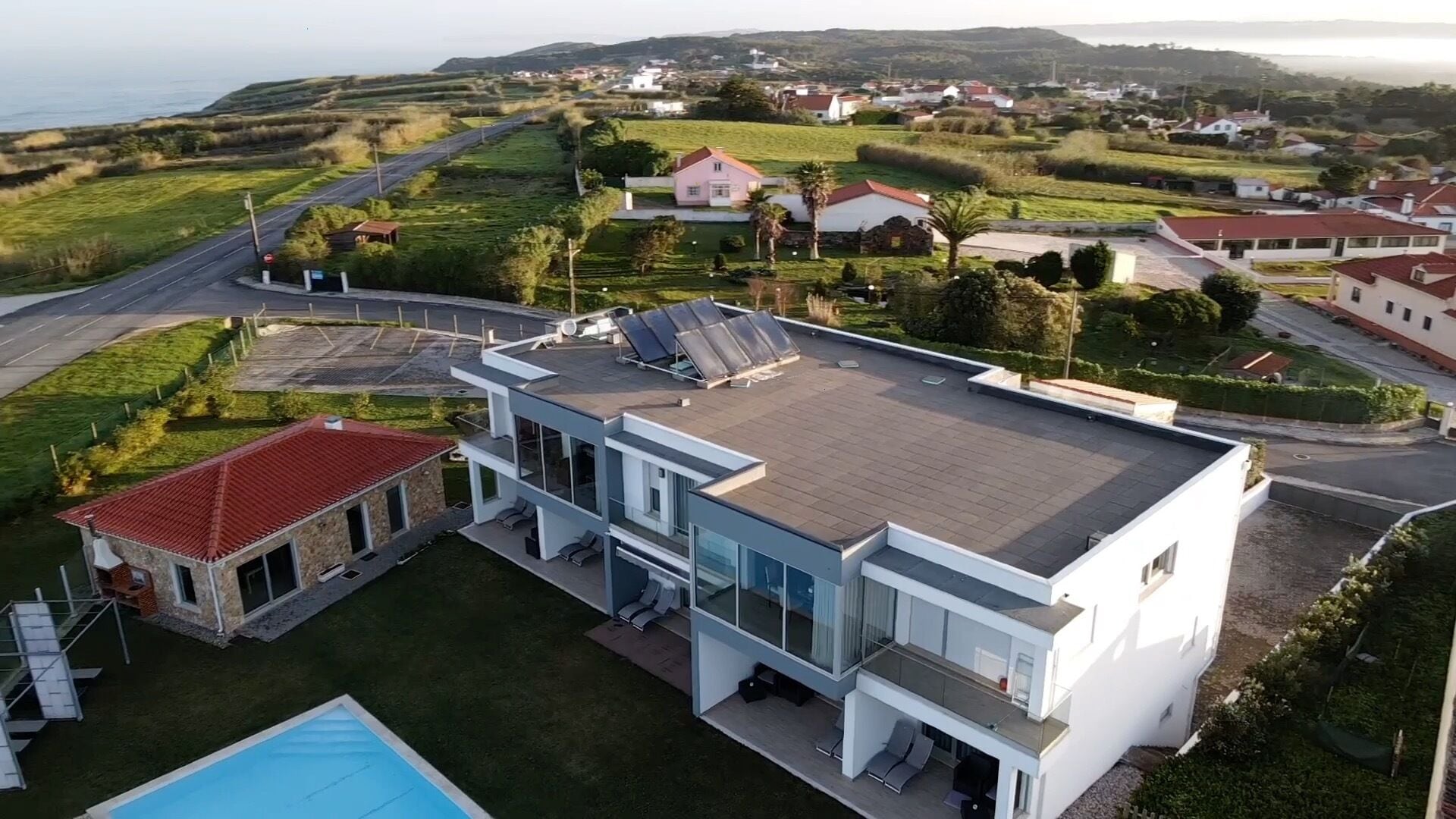 Une maison moderne à deux étages, dotée d’un grand toit-terrasse, d’une piscine et offrant une vue sur le paysage environnant.