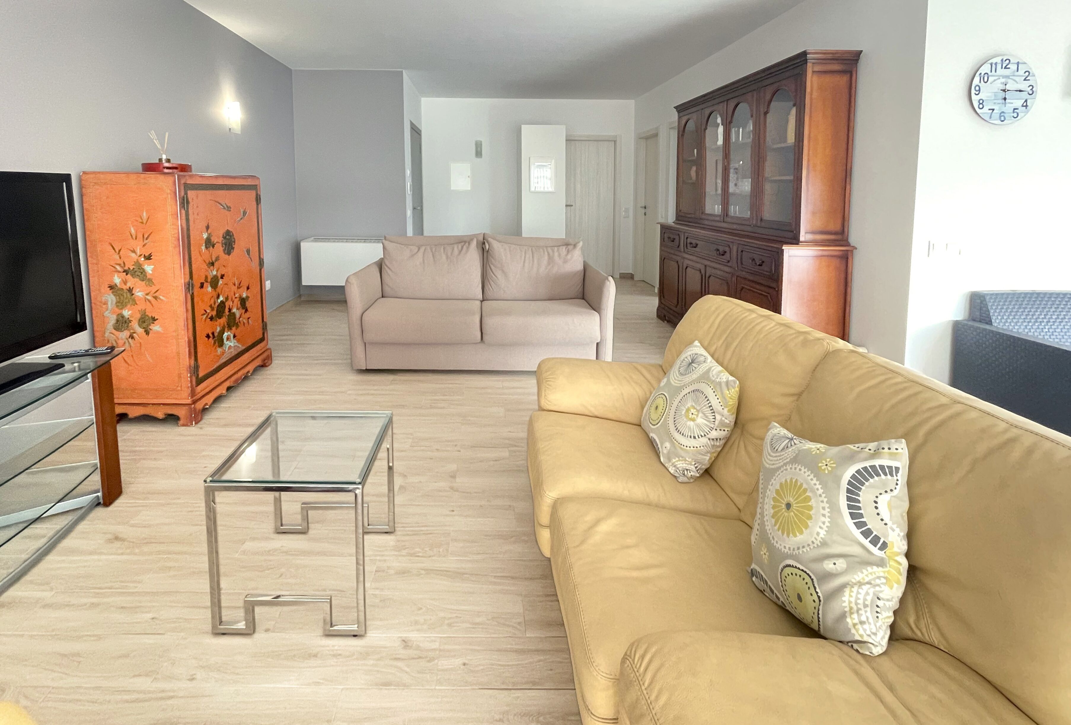 A living room with a beige sofa, a glass coffee table, a television, and a wooden cabinet.