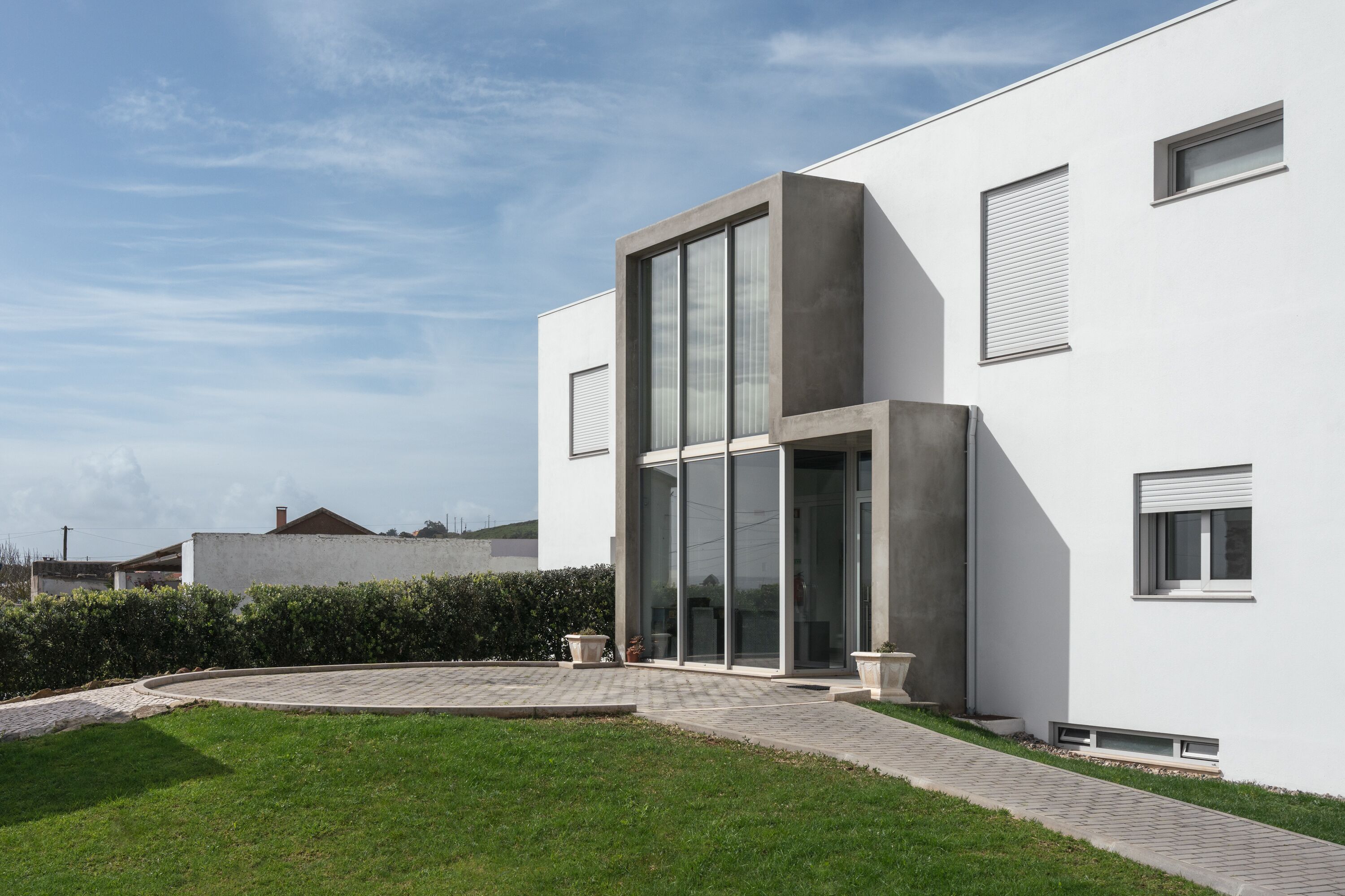 A modern building with a large glass entrance, a paved driveway, and a well-maintained lawn.