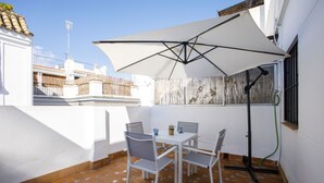 Un patio con una mesa y sillas blancas, una sombrilla grande y suelo de baldosas.