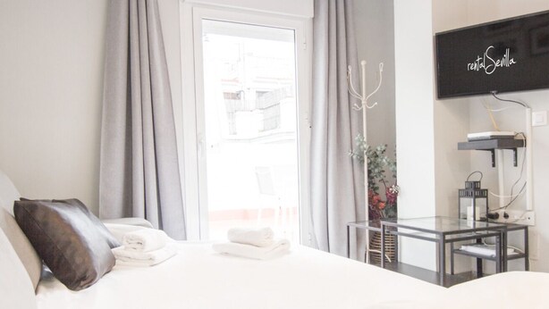 Habitación de hotel con cama, una mesita de noche con lámpara, televisión y vistas al exterior.
