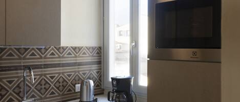 A modern kitchen with a stainless steel sink, a kettle, a coffee maker, and a microwave.