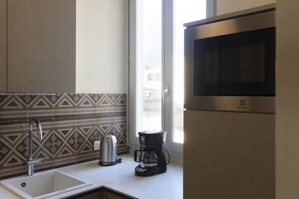 Une cuisine moderne équipée d’un évier en acier inoxydable, d’une bouilloire, d’une machine à café et d’un four à micro-ondes.