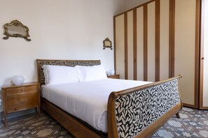 A neatly made bed with a patterned headboard, a wooden nightstand with a drawer, and a wardrobe with vertical panels. - Fossi Elegant Apartment (Firenze)