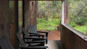A wooden deck with black chairs, a window overlooking a garden, and a door.