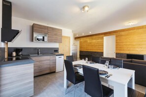 A modern kitchen with built-in appliances, a dining area with a white table and black chairs, and wooden paneling on the walls.