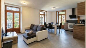 A modern apartment with a sofa, dining table, chairs, and a kitchen area.