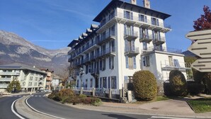 A multi-story hotel with balconies, a curved road, and mountains in the background.