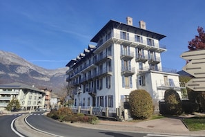 A multi-story hotel with balconies, a curved road, and mountains in the background.