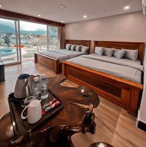 A hotel room with two beds, a coffee table with a tray of breakfast items, and a view of a swimming pool and mountains.