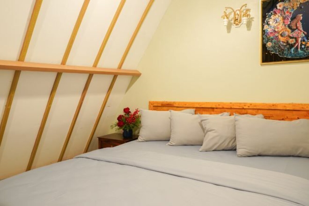 A bedroom with a sloped ceiling, a wooden headboard, and a bed with multiple pillows.