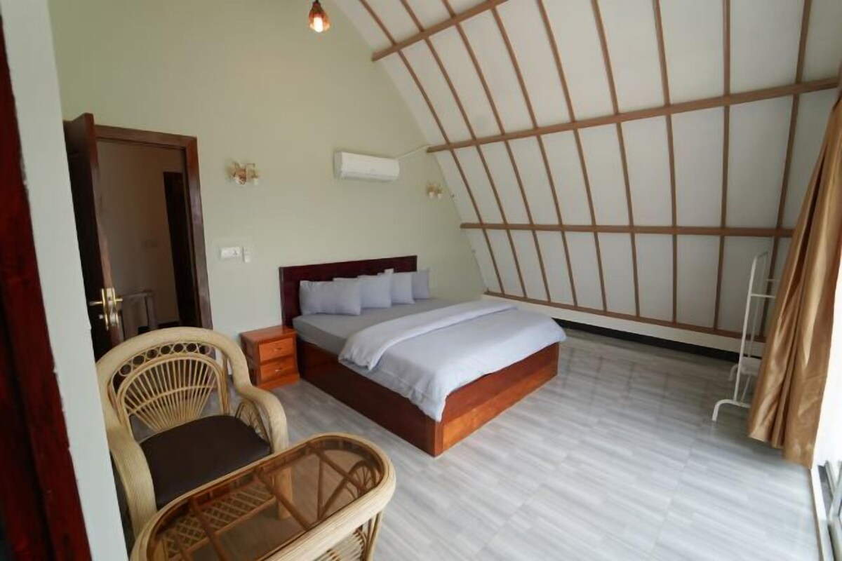 Un dormitorio con cama, mesitas de noche, una silla y estructura de techo de madera.