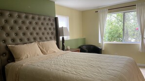 Uma cama bem arrumada com cabeceira estofada, mesa de cabeceira com abajur e janela com cortinas.