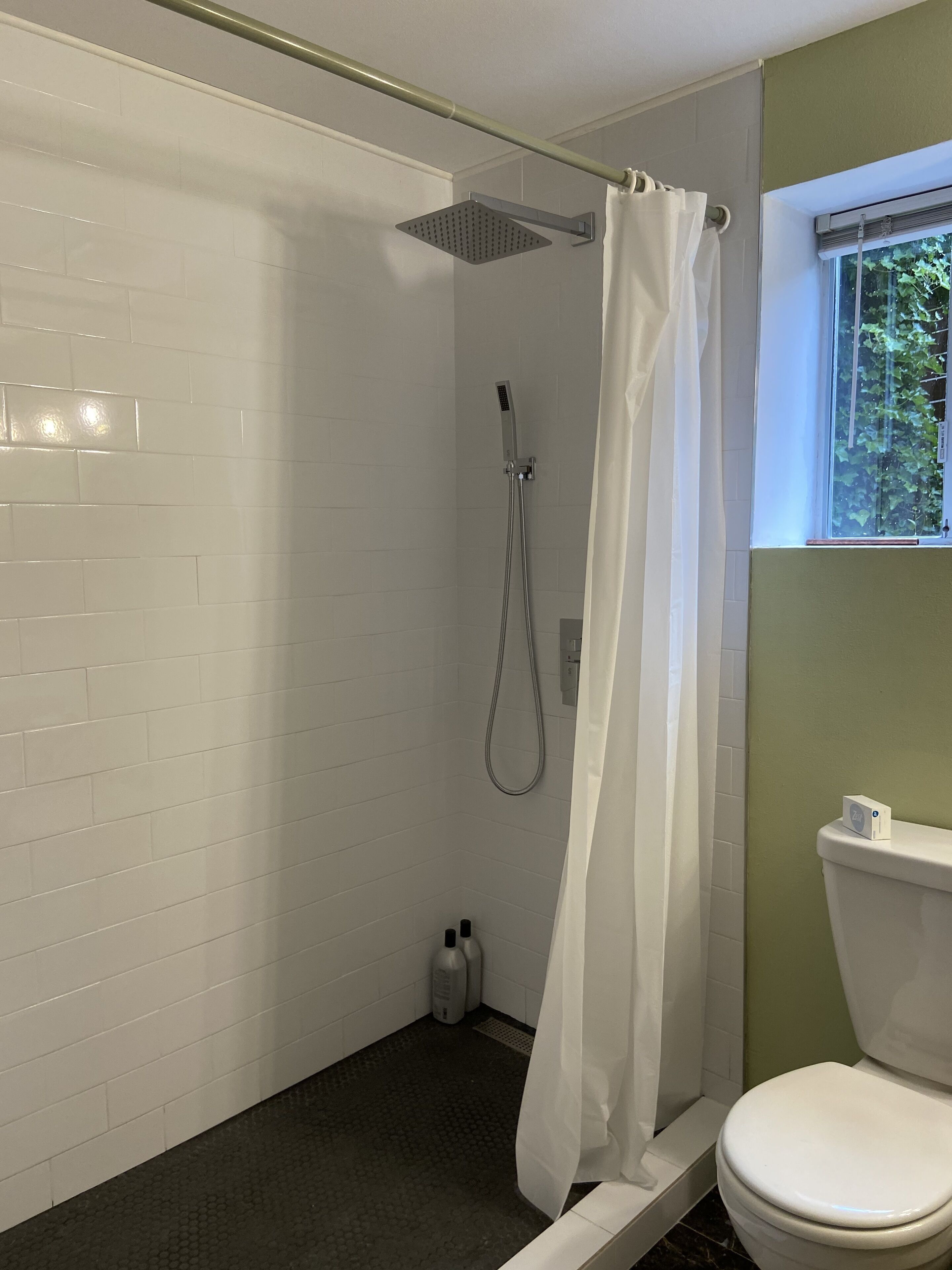 Un baño con ducha, inodoro y ventana.