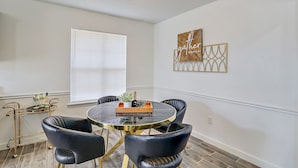 Un comedor con una mesa redonda, sillas de cuero negro, un carrito de metal dorado y negro, y un aplique de pared.