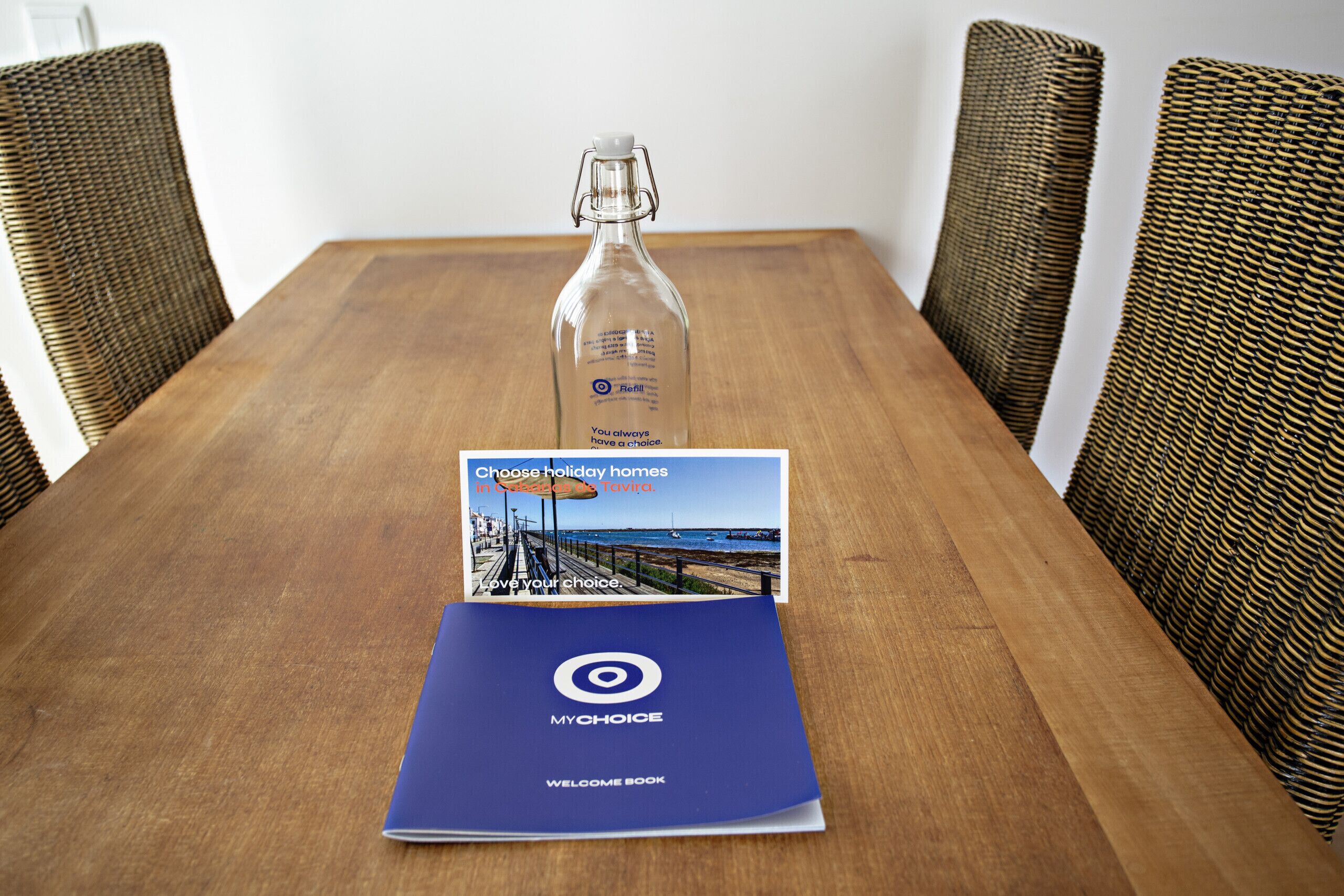 A wooden table with a bottle of water, a brochure, and a welcome book.