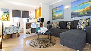 A living room with a gray sofa, a dining table with a patterned tablecloth, and artwork on the walls.