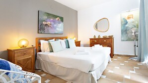 A hotel room with a large bed, wooden headboard, bedside tables with lamps, a wooden dresser, and two paintings on the walls.