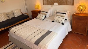 A bedroom with a bed, bedside tables, a lamp, a wall-mounted light, and a decorative wall piece. - Villa with outdoor spaces (Cabanas de tavira)