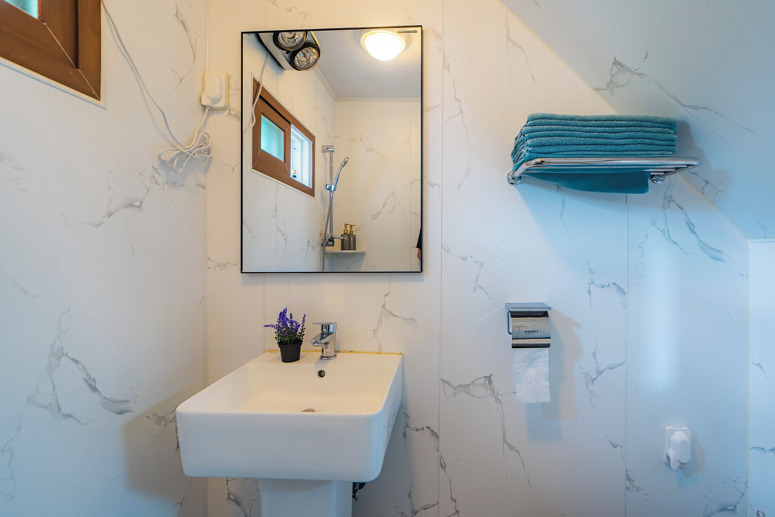 A bathroom with a white sink, a mirror, a towel rack, and a marble-patterned wall.