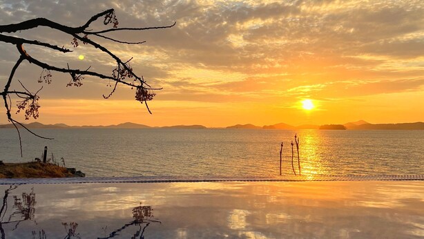 A sunset over a calm sea with a clear sky and distant mountains. - SkyStarSea Pension (Muan)