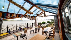 An outdoor dining area with a view of the water, wooden furniture, and hanging light fixtures. - SkyStarSea Pension (Muan)