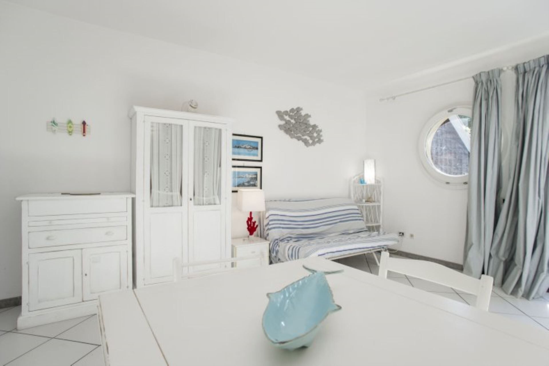 Une chambre à coucher comprenant un lit, une commode, une table de chevet, une fenêtre avec des rideaux et un élément de décoration murale.