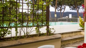 A poolside area with a view of the pool, a pergola with climbing plants, and a fence.