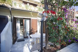 A patio with a table and chairs, a glass door leading to an interior space, and a garden with various plants and flowers.