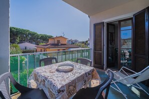 A balcony with a table, chairs, and a view of houses and trees.