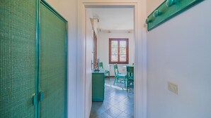 A hallway leading to a dining area with a window, a green cabinet, and a chair. - APP.TI STELLA MARINA - STELLA MARINA 3 (Marina di Campo)