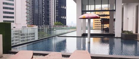 A modern building with a swimming pool, lounge chairs, and a large umbrella.