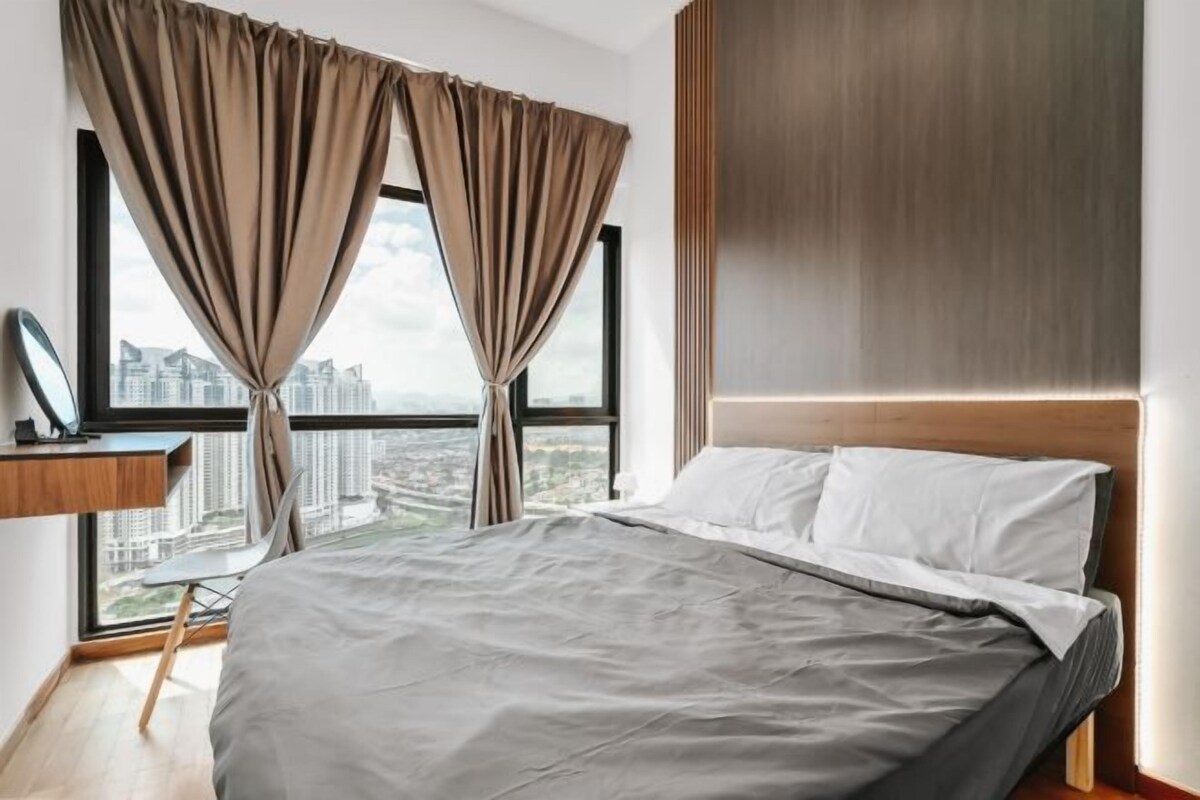 Une chambre moderne avec un grand lit, un bureau et une vue sur le paysage urbain, grâce à de grandes fenêtres.