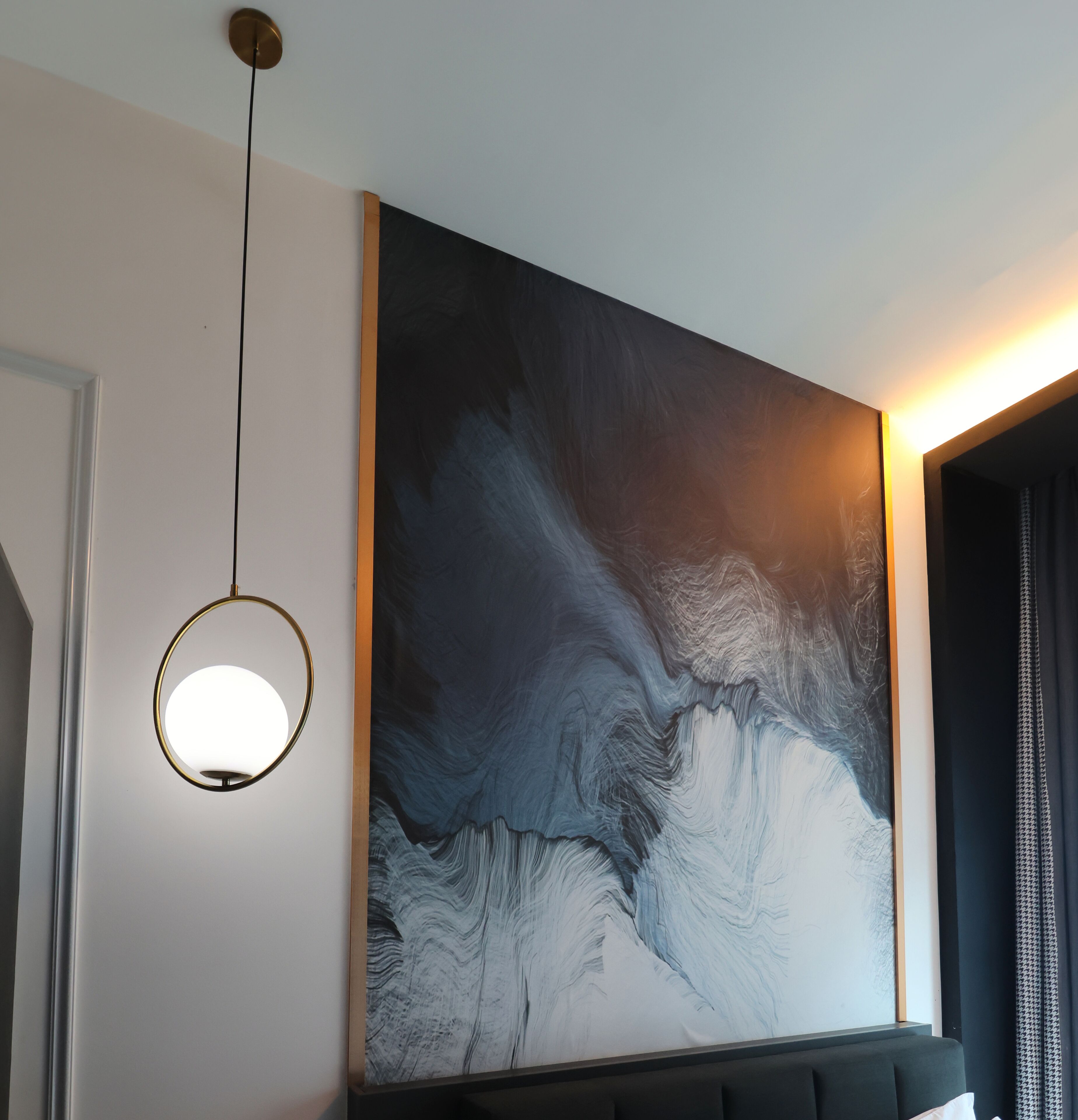 Ein modernes Interieur mit einem großen abstrakten Gemälde an der Wand, einer runden Pendelleuchte und einem dunkelgrauen Sofa.