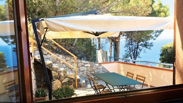 Une terrasse avec une table et des chaises, un mur en pierre et une vue sur la mer.