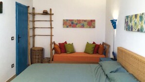 Une chambre à coucher avec un lit, un canapé, une échelle, une lampe et un mur orné d’un tableau représentant des motifs floraux.