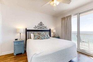 Quarto com cama grande, duas mesas de cabeceira com luminárias, ventilador de teto e varanda com vista.