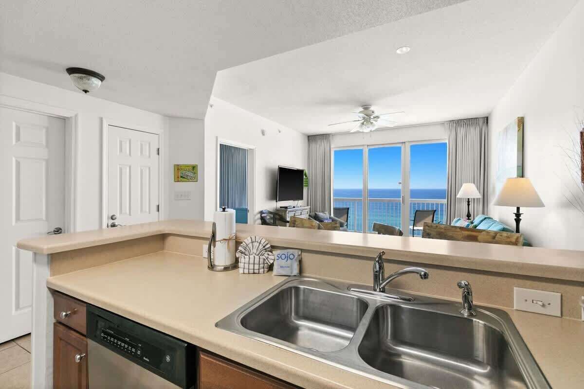 Een moderne keuken met een dubbele spoelbak, een vaatwasser en een groot raam met uitzicht op de oceaan.