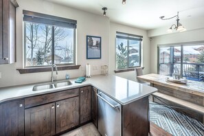 A modern kitchen with dark wood cabinets, a stainless steel island, and large windows offering views of a snowy landscape.