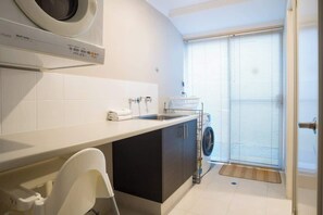 Cocina compacta con lavadora, lavamanos y ventana con persianas.
