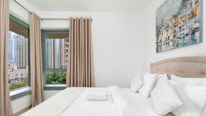 Een hotelkamer met een groot bed, beige gordijnen, uitzicht op de stad en een schilderij aan de muur.