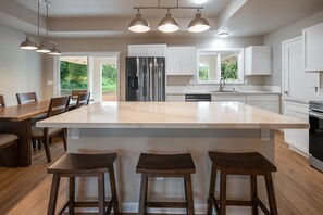 Une cuisine moderne dotée d’un grand îlot central, de meubles blancs, d’appareils électroménagers en acier inoxydable et d’un coin repas avec des chaises et une table en bois.